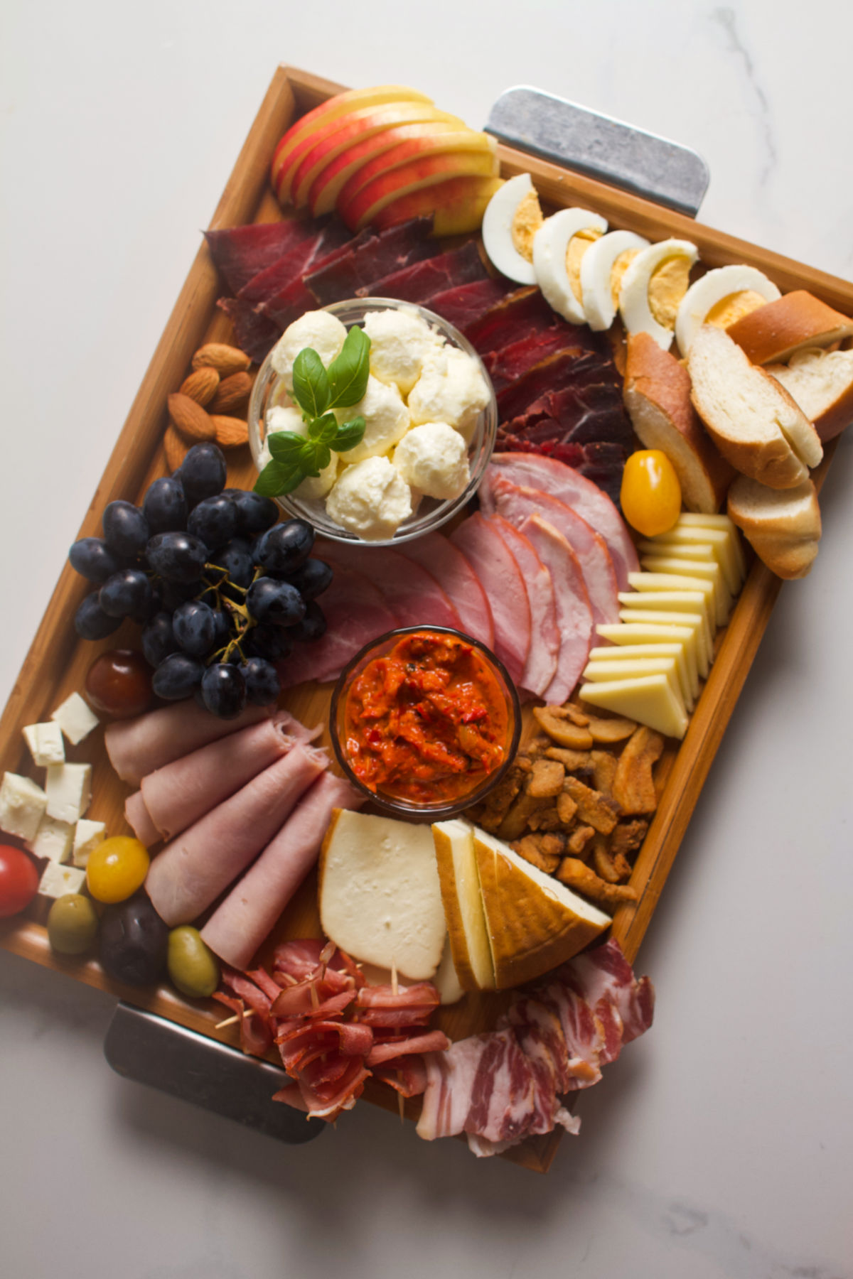 Overhead photo of a meat and cheese wooden tray platter on a gray background.