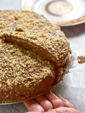 Cake being cut and a hand holding it on the bottom.