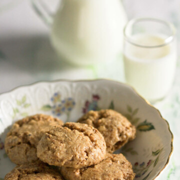A plate with five walnut cookies, a pitcher with milk and a small glass of milk on a marble background.