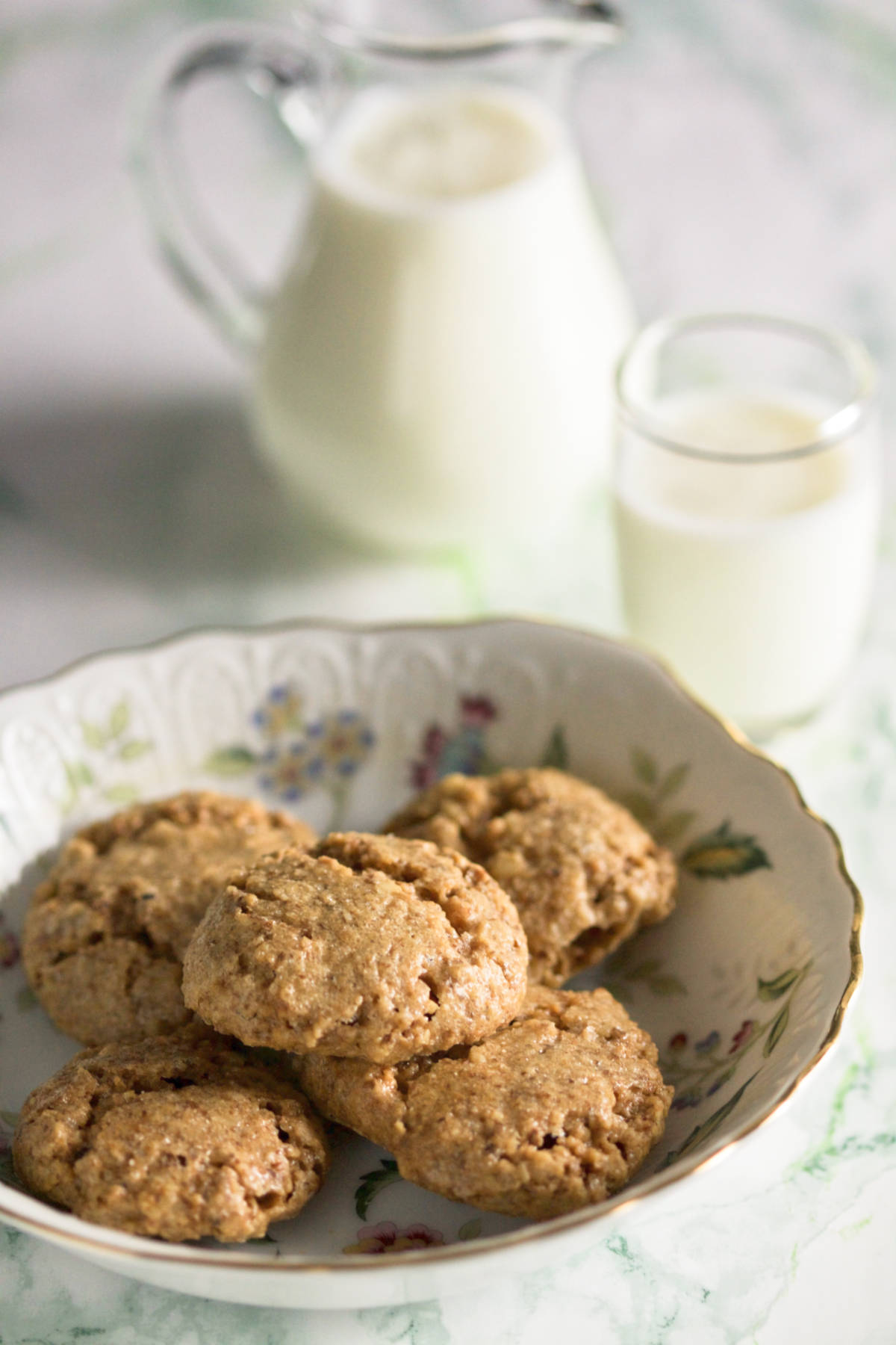 A plate with five walnut cookies, a pitcher with milk and a small glass of milk on a marble background.