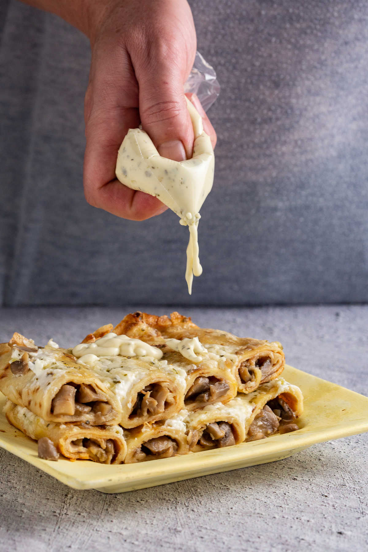 Eight crepes on a plate, and a hand holding tartar saauce. 