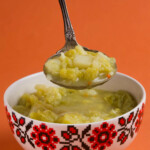 A bowl with savoy cabbage soup and a spoonful above being held by a hand.