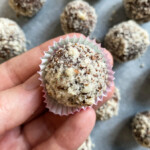 A hand holding a fig ball in air above other fig balls on table.