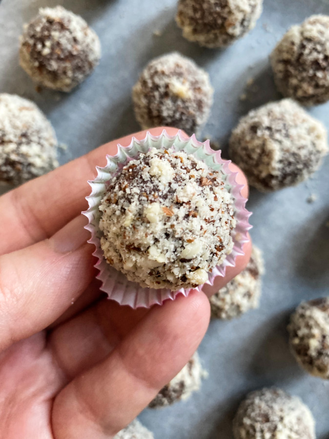 A hand holding a fig ball in air above other fig balls on table.