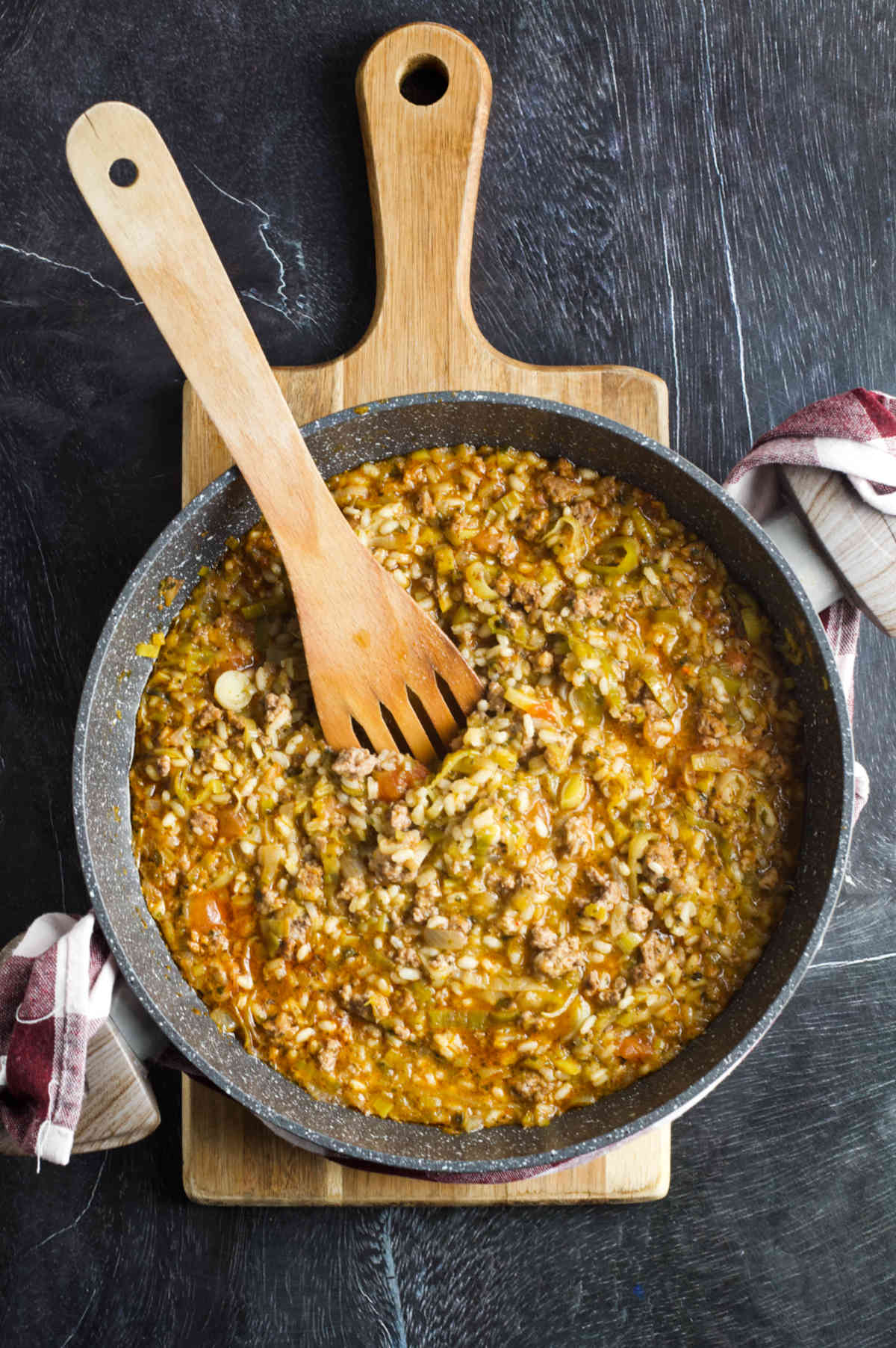A pan with risotto on a cutting board and a wooden spoon in the pan on a gray background. 
