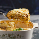Serving of lasagna on a ladle, and lasagna pan on a gray background.