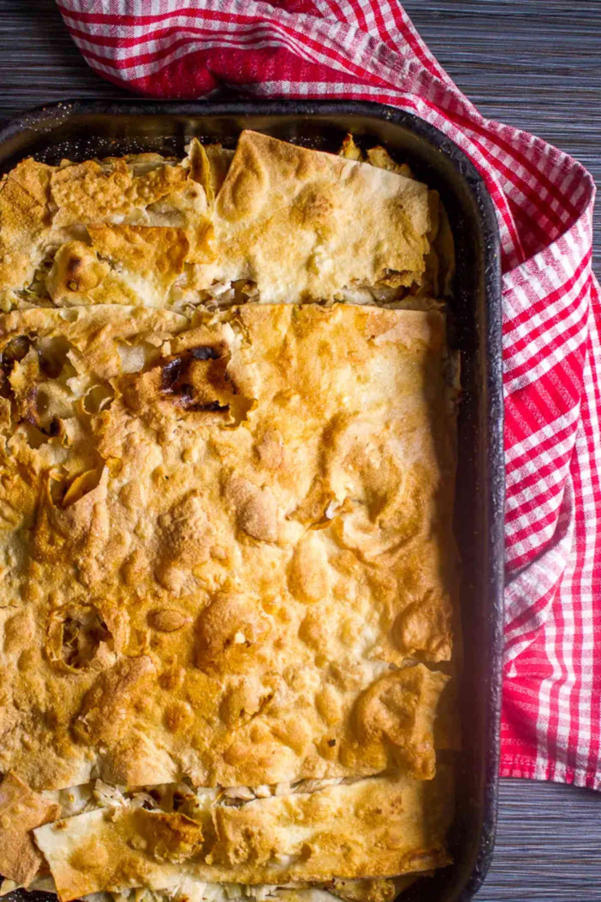 Overhead photo of a pan holding chicken tortilla pie with a plaid red and white kitchen towel. 