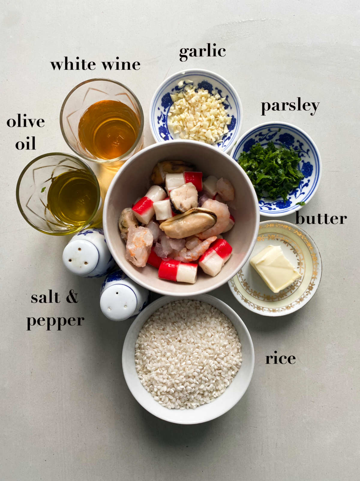 Ingredients from above on a gray table: white wine, olive oil, garlic, parsley, butter, rice, salt and pepper. 