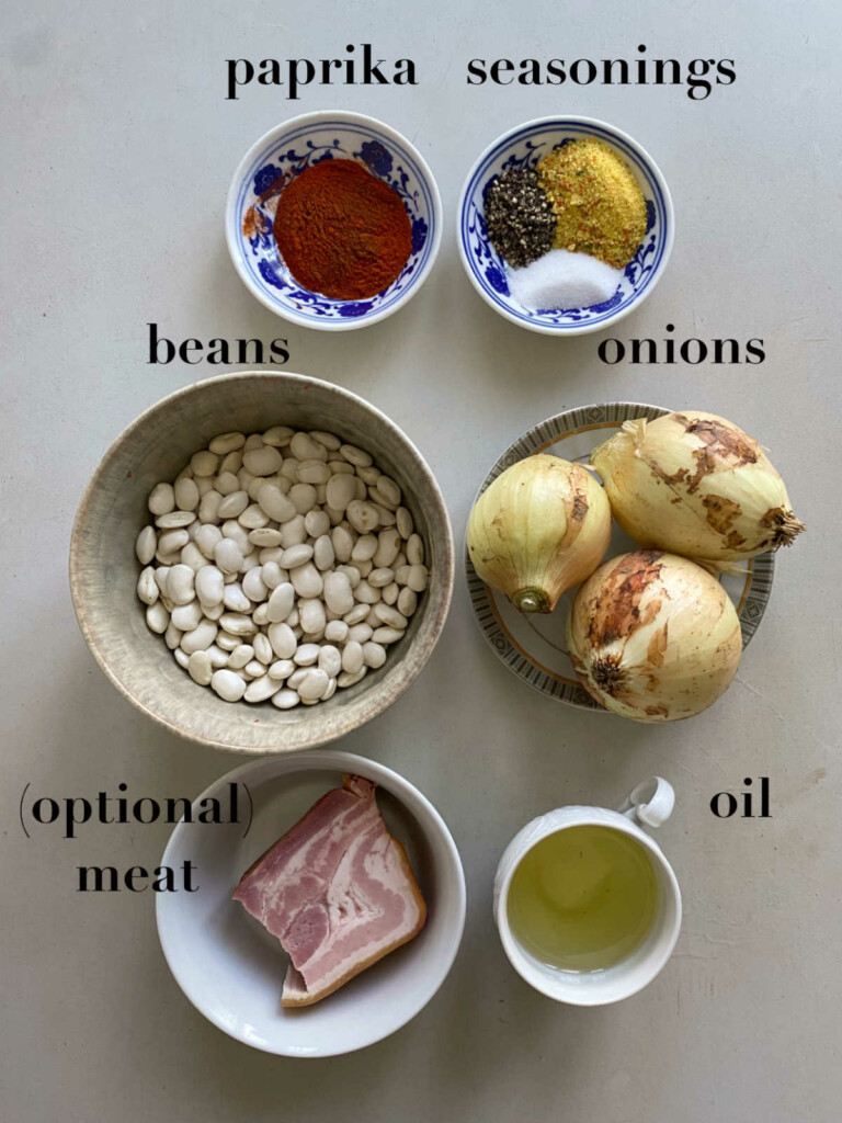 Ingredients in different bowls: paprika, seasonings, beans, onion, oil and meat. 