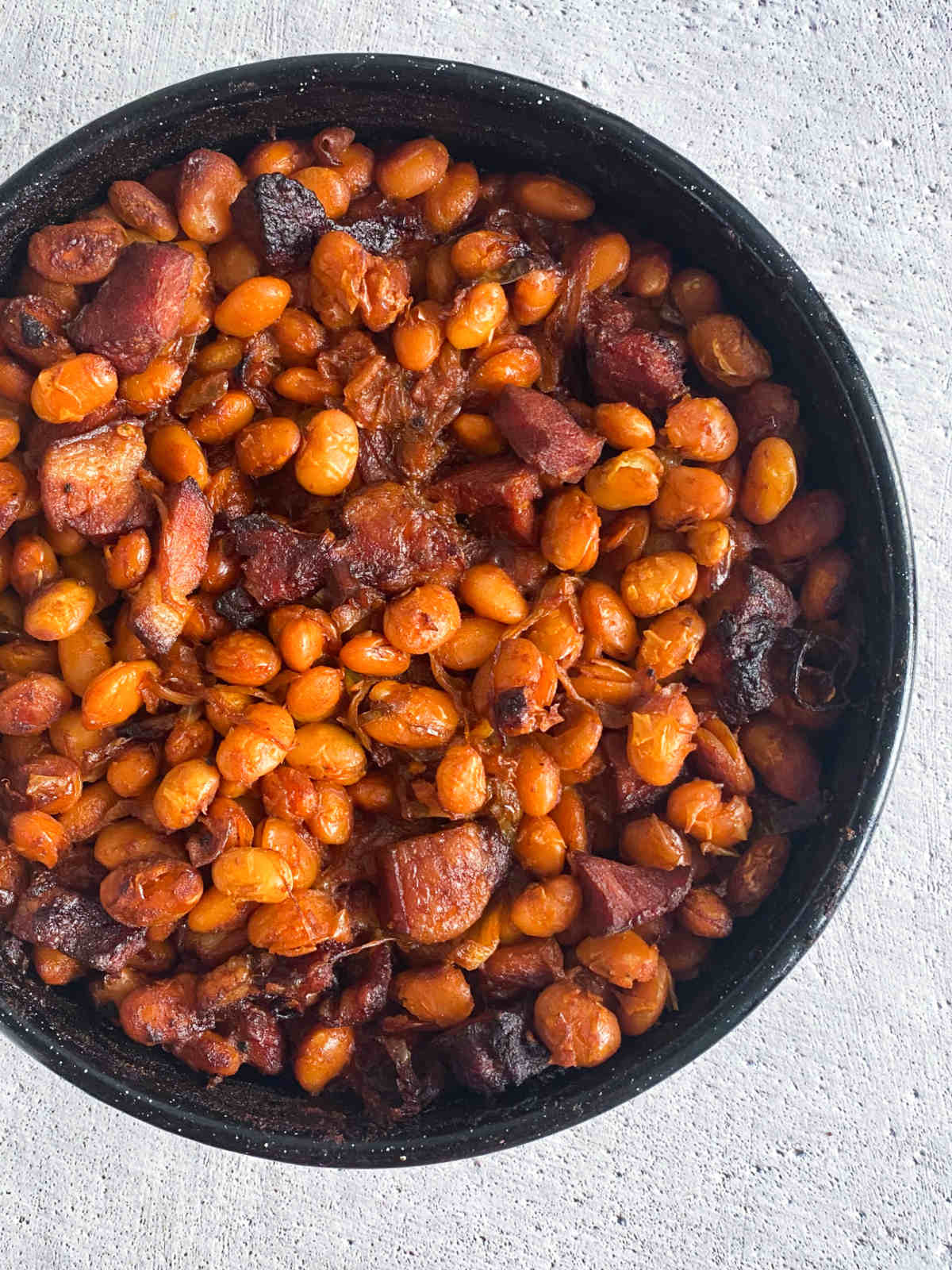 Baked beans in a black pan on a marble tabletop, overhead.