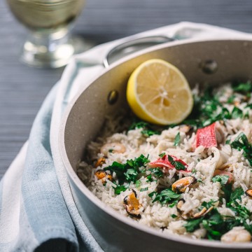 Pan with seafood risotto on a gray background with a kitchen towel.