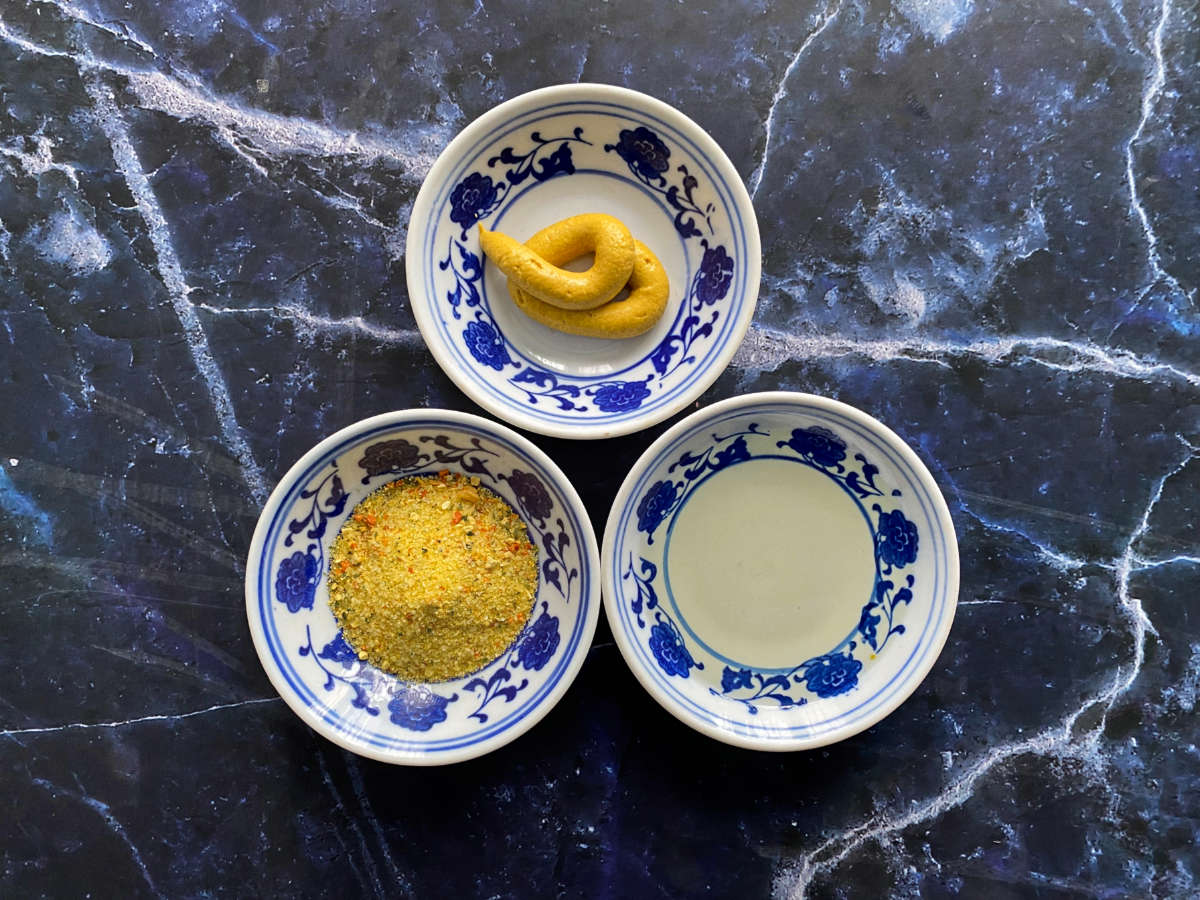 Three small white and blue plates with different ingredients (Vegeta, mustard and oil) on dark blue marble background. 