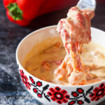 Pepper sauce in a white bowl on a table and a pepper in the background.