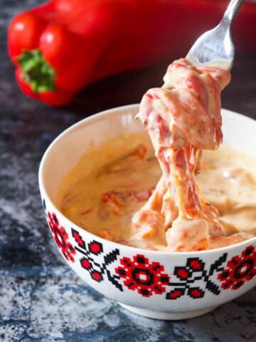 Pepper sauce in a white bowl on a table and a pepper in the background.