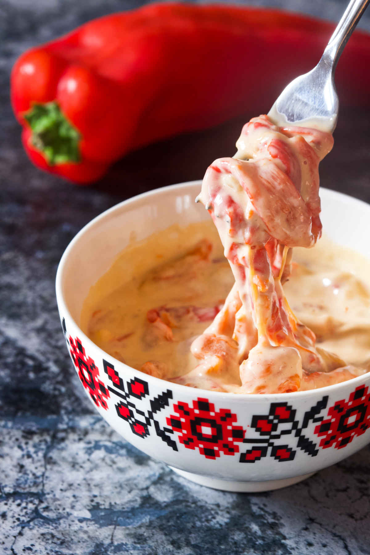 Pepper sauce in a white bowl on a table and a pepper in the background.