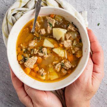 Two hands holding a bowl of stew.