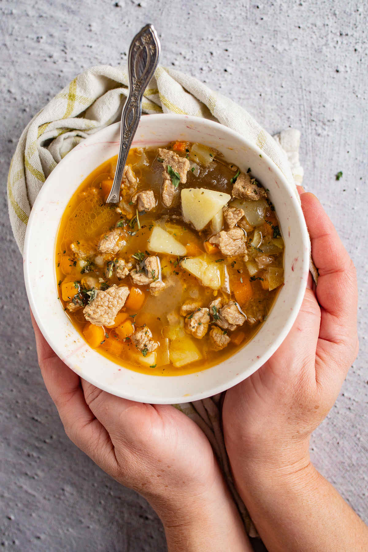 Two hands holding a bowl of stew. 