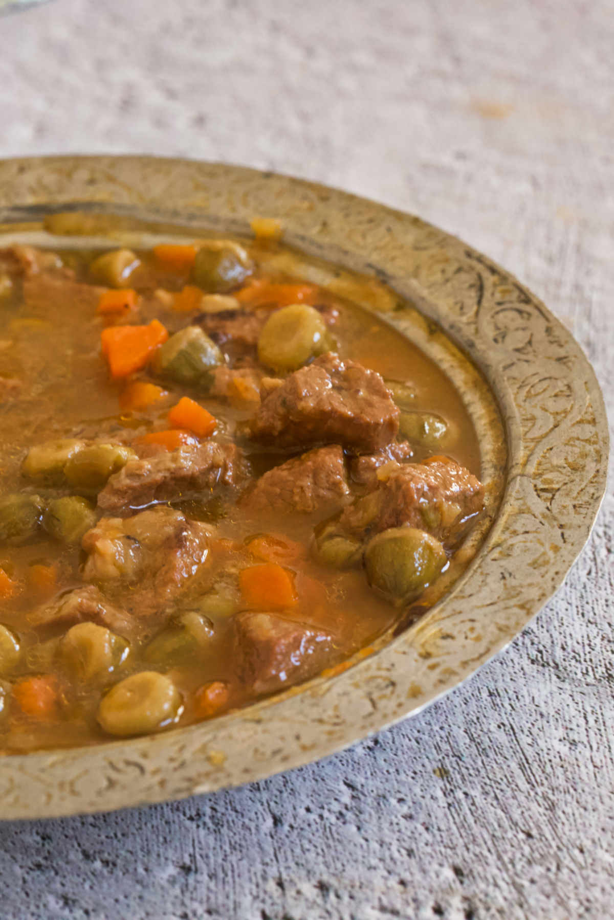 Silver bowl filled with a stew, on a gray background. 