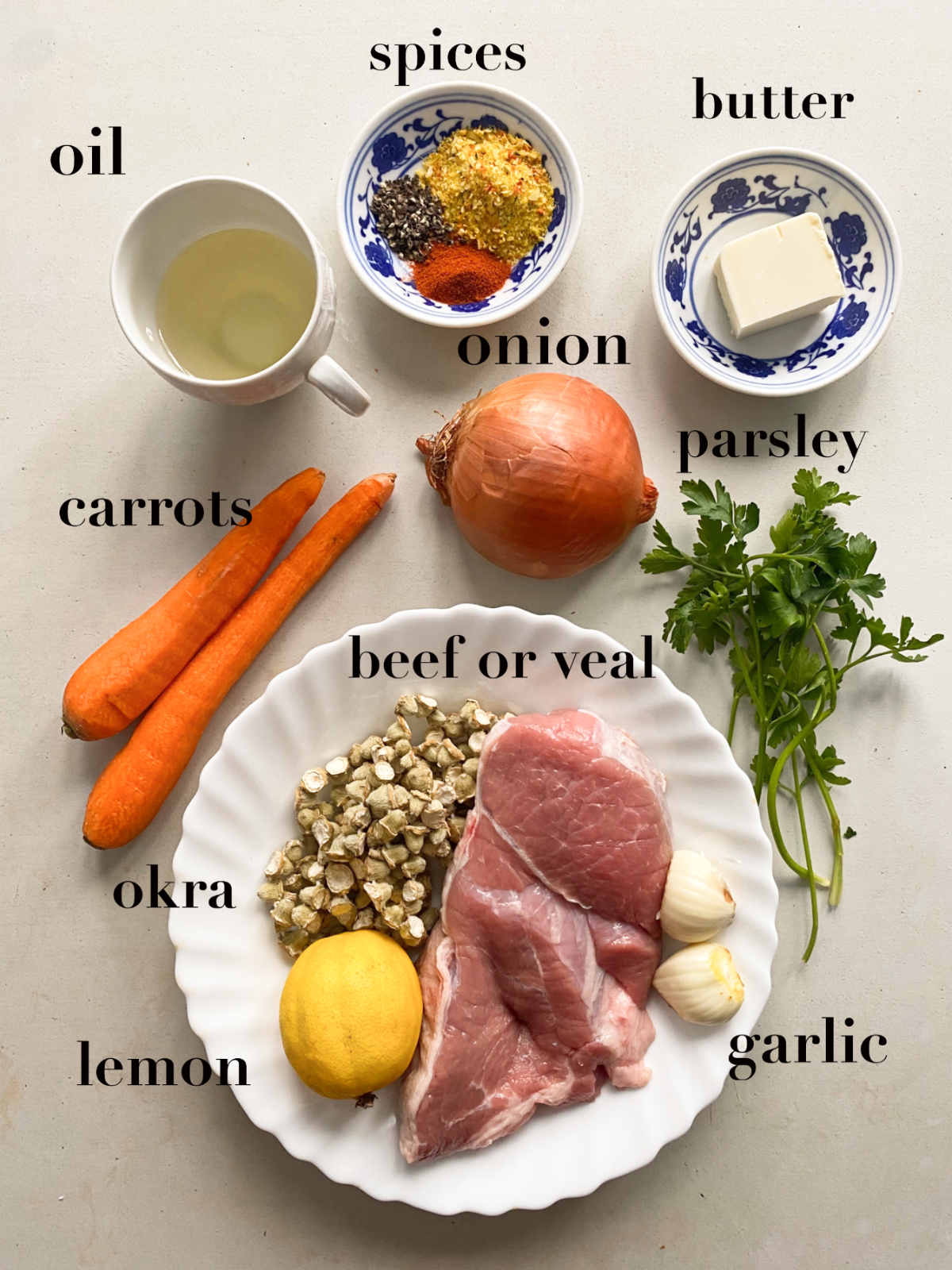 Ingredients for stew on a white background: oil, spices, butter, carrots, veal, onion, parsley, garlic, okra, lemon. 