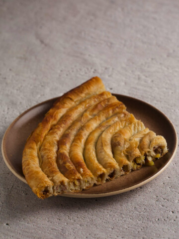 Quarter of a burek pie on a plate on gray background.