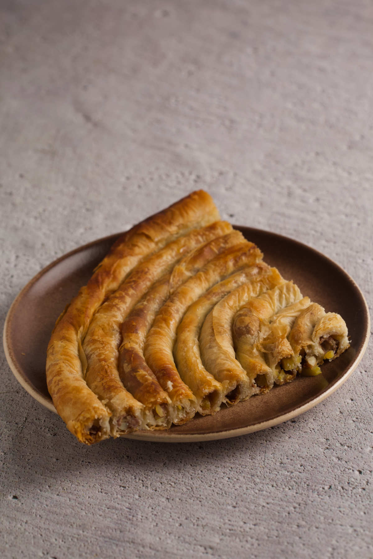 Quarter of a burek pie on a plate on gray background. 