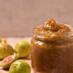 Jar with fig jam, and figs spread on the pink table.