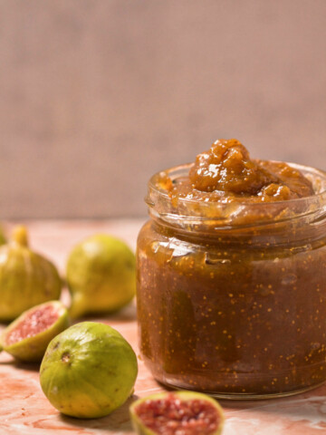 Jar with fig jam, and figs spread on the pink table.