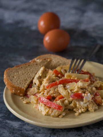 A plate with eggs and peppers (satarash) with two halves of integral bread with a fork and two eggs on a dark marble background.