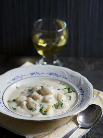 A bowl of gnocchi, glass of wine and a spoon.