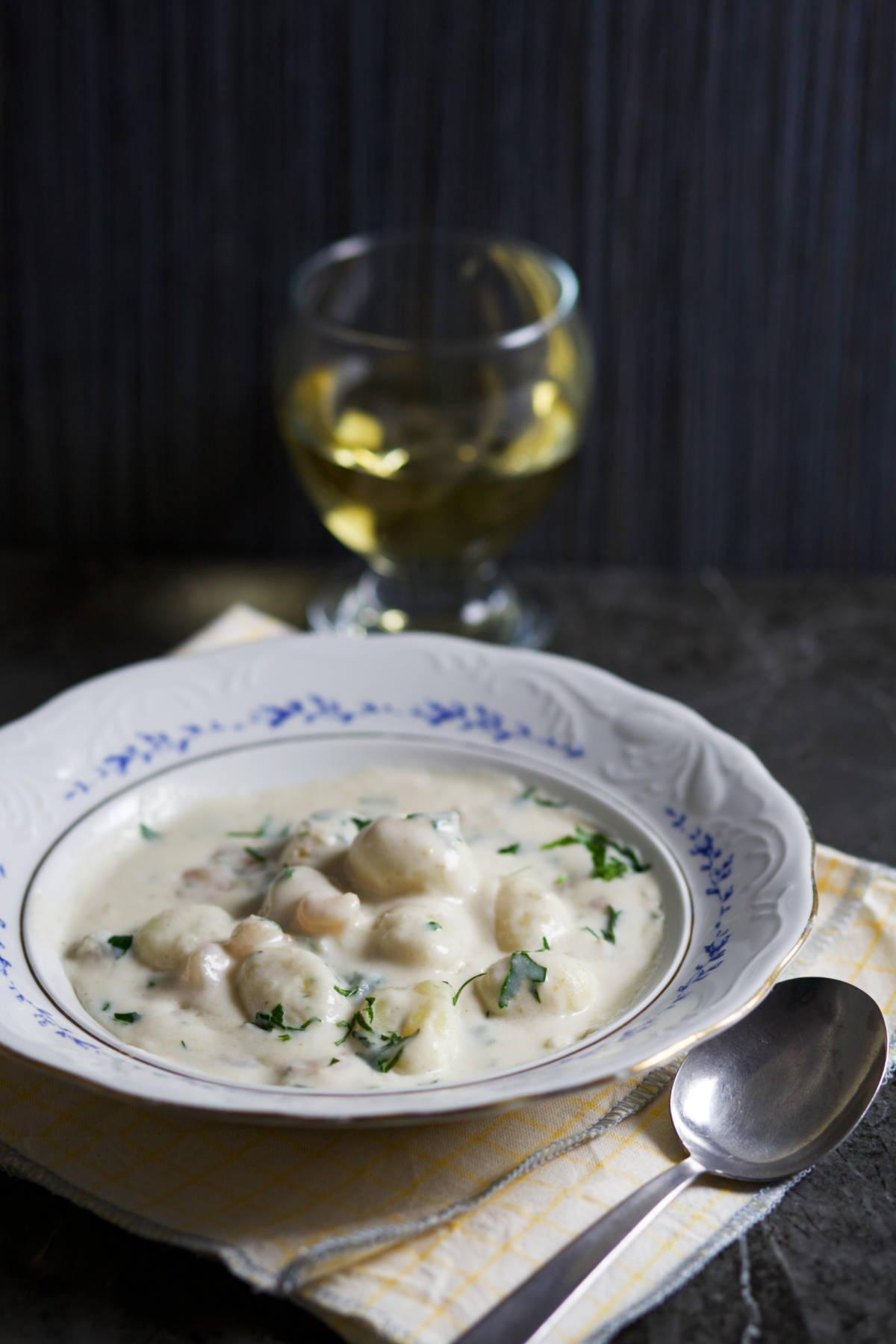 A bowl of gnocchi, glass of wine and a spoon.