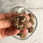 A hand holding a chocolate ball above a glass bowl full of chocolate balls.