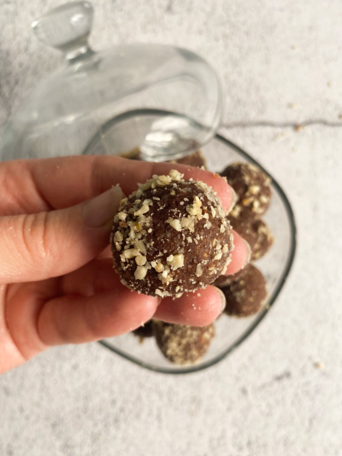 A hand holding a chocolate ball above a glass bowl full of chocolate balls. 