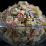 Glass bowl full of Russian salad on black background.