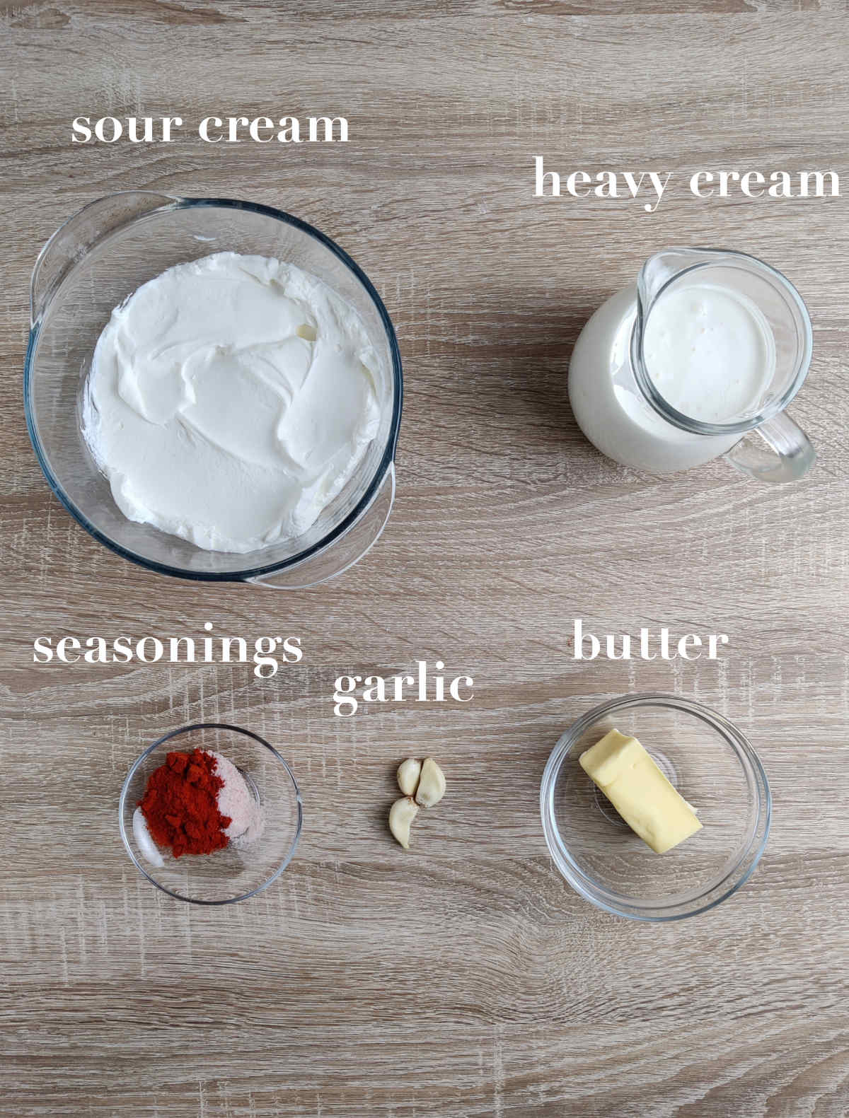 Ingredients for the sauce on a wooden table photographed from above (sour cream, heavy cream, seasonings, butter, garlic). 