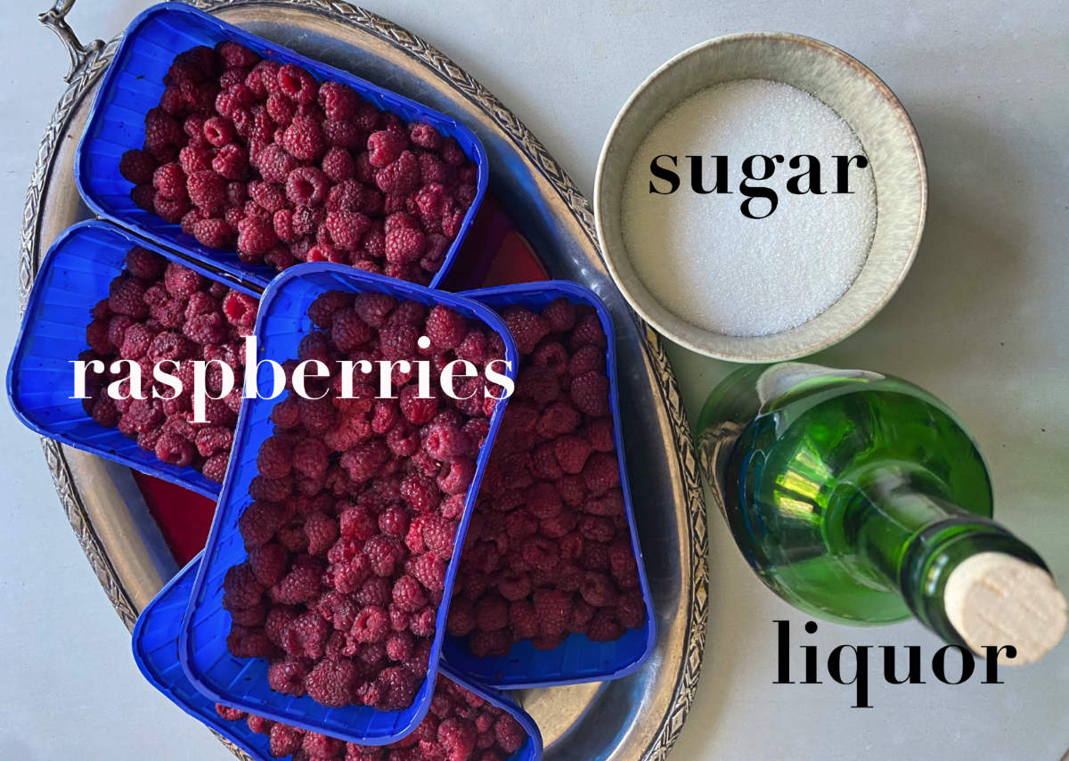 Raspberries on a tray, sugar in a bowl and liquor in a green bottle on a gray background. 