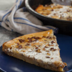 Piece of pie on a blue plate, a napkin and a pan with pie in the back, on a gray background.
