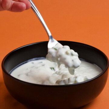 A hand holdling a fork with scallion salad above a black bowl filled with salad on an orange background.