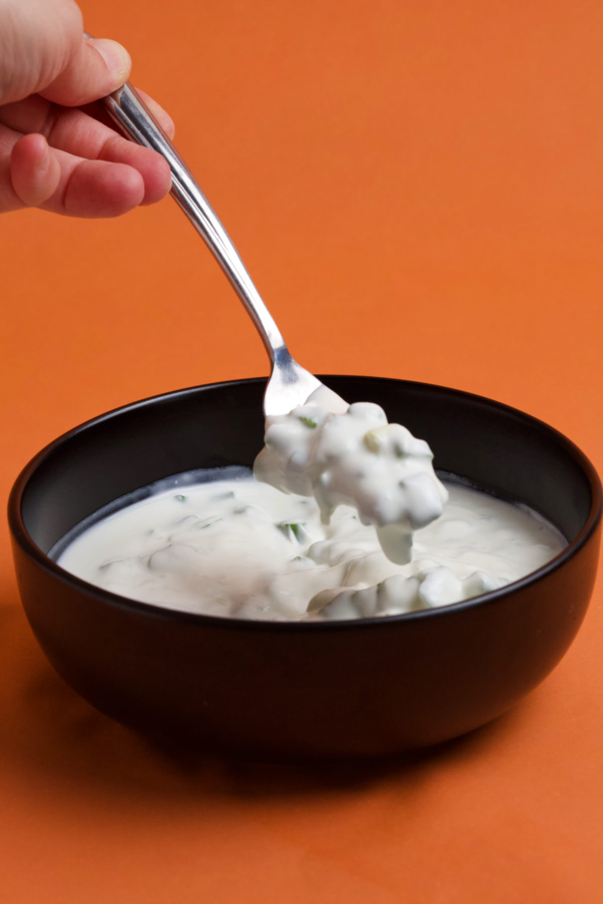 A hand holdling a fork with scallion salad above a black bowl filled with salad on an orange background.
