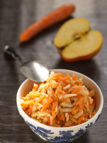 Bowl with carrots and apple, and carrot and apple and a spoon on a table.