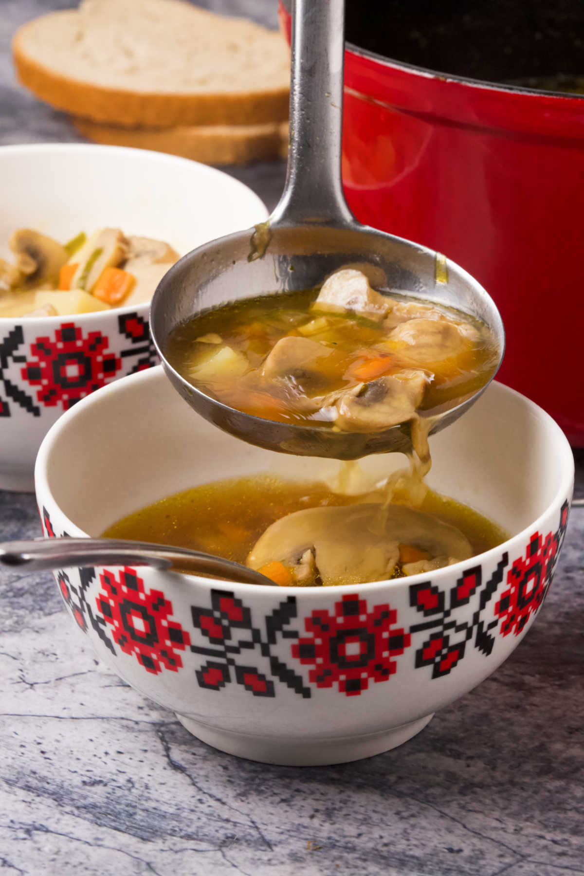 Two bowls of soup, and a ladle full of soup pouring it into one of the bowls.