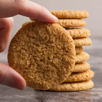 A hand holding a cookie and several in the background.