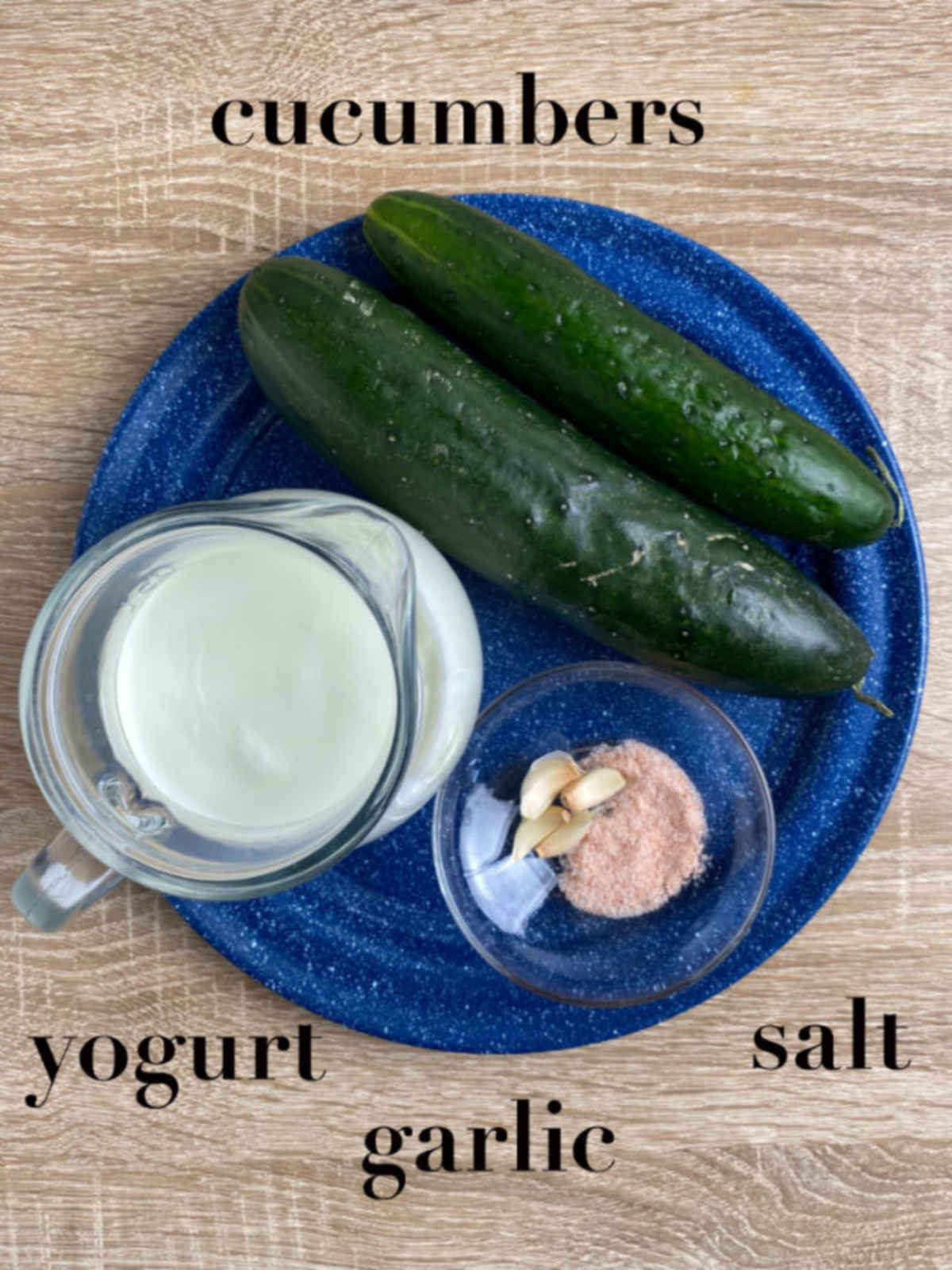 Yogurt, cucumbers, salt and garlic on a blue plate overhead, on a table.