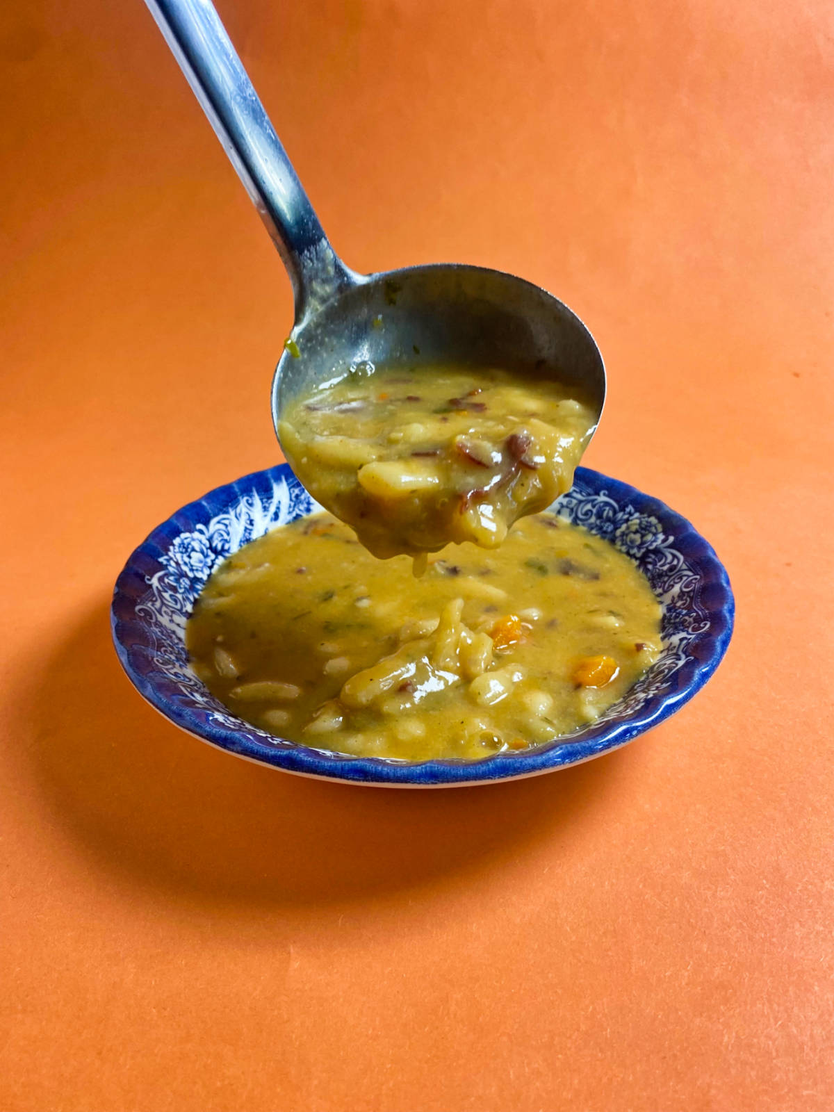 A ladle holding bean soup above the blue bowl, on an orange background.