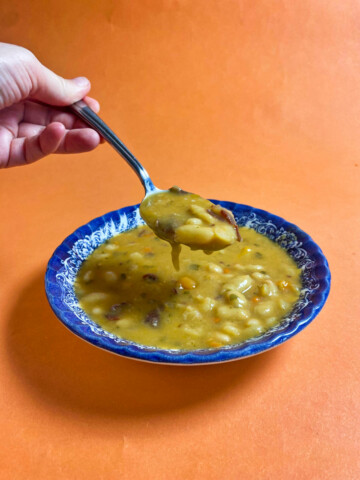 A ladle holding bean soup above the blue bowl, on an orange background.