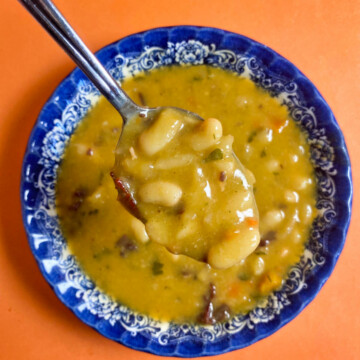 A spoon holding bean soup above the blue bowl, on an orange background.
