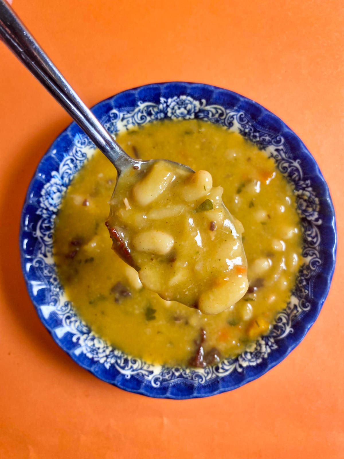 A spoon holding bean soup above the blue bowl, on an orange background.