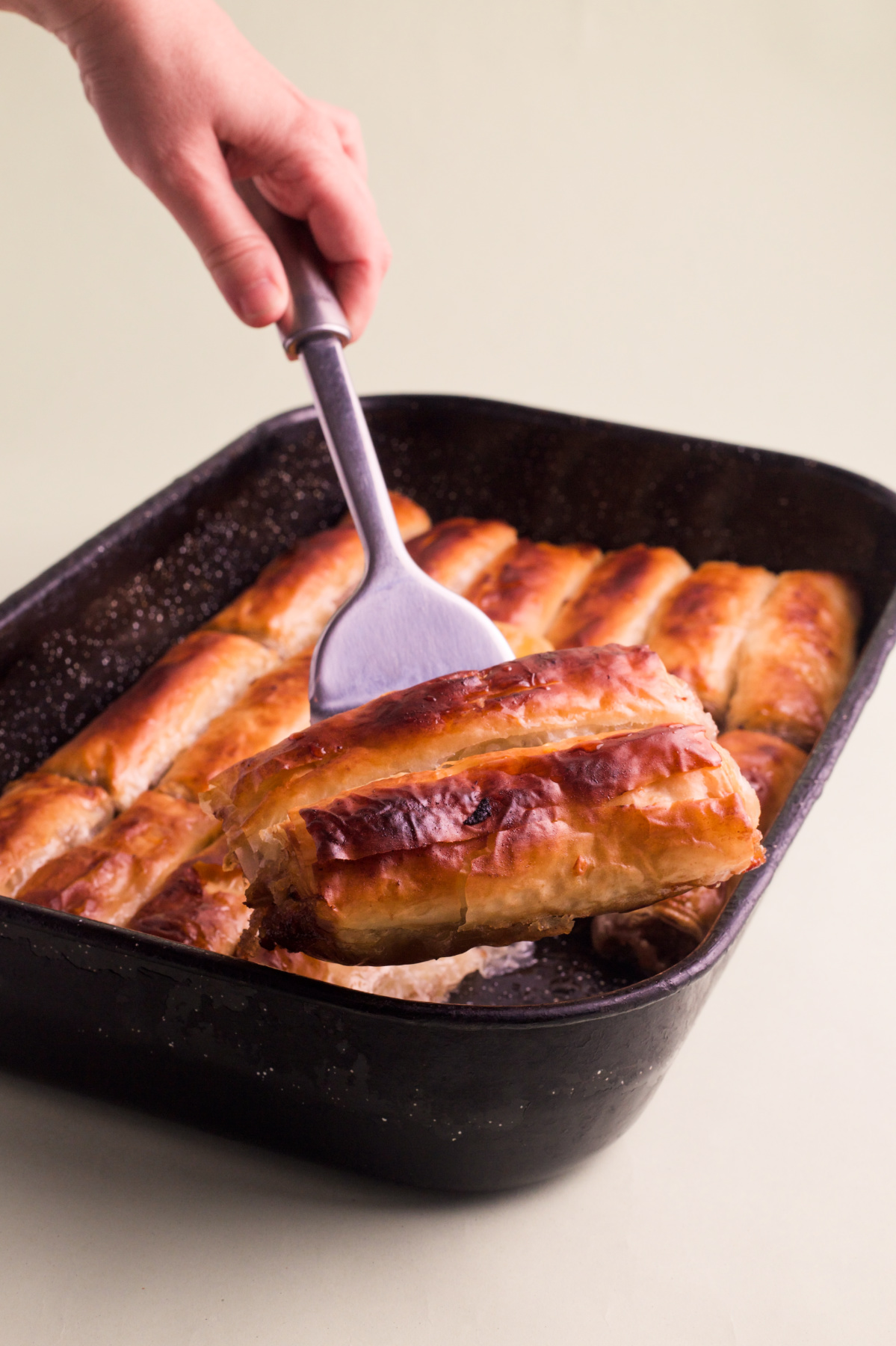 A hand holding two pieces of apple pie above a pan of apple pie.